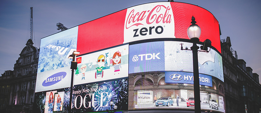 Gebouw met enorme billboards erop die grote merken adverteren. Waaronder Coca Cola Zero, TDK, Samsung en McDonalds.